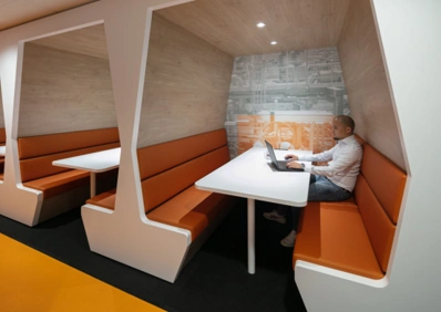 Man werkt op een laptop in een moderne werkruimte met oranje zithoeken aan de Karel Doormanweg.